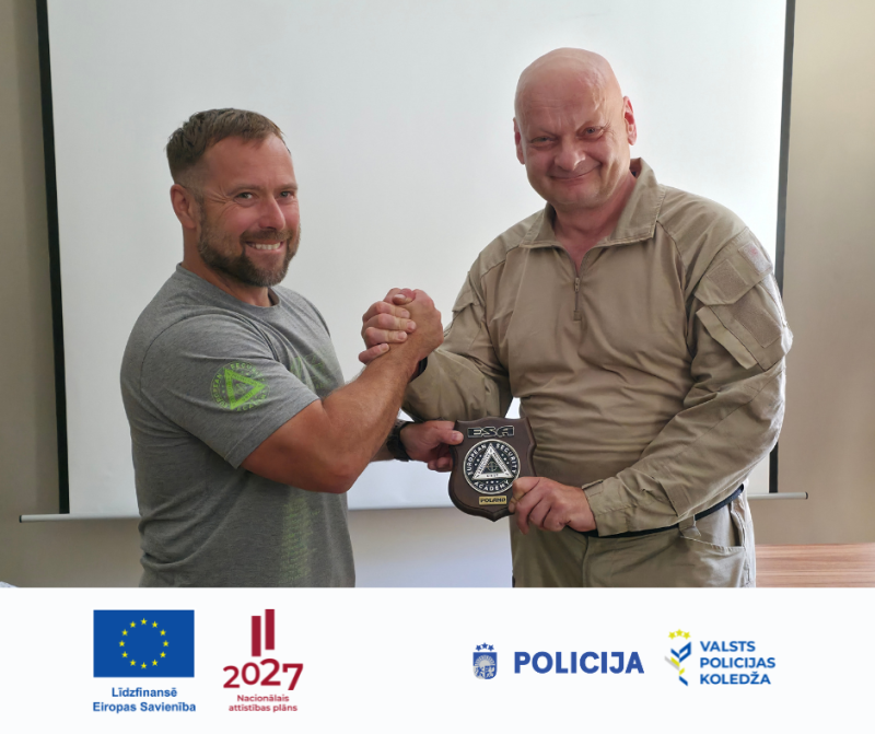 Divi tiesībaizsardzības iestāžu pārstāvji sarokojas, pasniedzot piemiņas plāksni ar apmācību organizācijas emblēmu