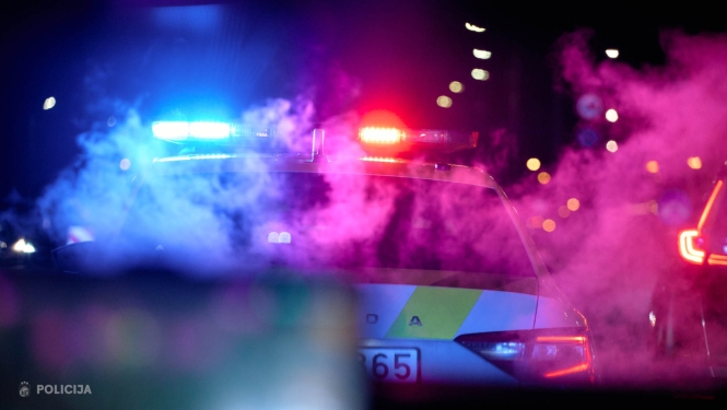 Tumšā diennakts laikā redzama Valsts policijas automašīna ar ieslēgtām zilām un sarkanām bākugunīm. Apkārt auto redzami krāsaini gaismas atspīdumi un dūmi, fonā, izplūdušas pilsētas gaismas