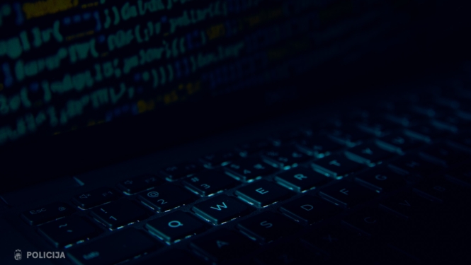 Tumšā, zilganā apgaismojumā tuvplānā redzama datora tastatūra, bet fonā izplūduši programmēšanas koda fragmenti