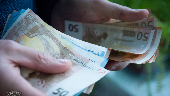 Redzamas 2 cilvēka rokas, kas skaita naudas banknotes. Redzami 50 un 20 eiro nomināli