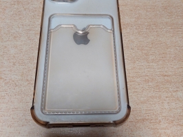 Apple mobilais telefons caurspīdīgā vāciņā fotografēts no priekšpuses, ar ieslēgtu ekrānu un no aizmugures uz gaišas koka virsmas