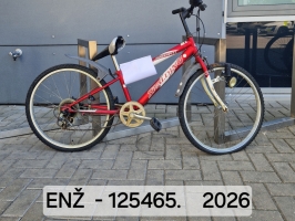 Sarkans bērnu velosipēds ar pelēku dakšu, baltām riepu malām, dubļu sargiem un priekšējo lukturi novietots velonovietnē pie ēkas.