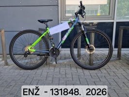 Tumši zils un zaļš kalnu velosipēds ar amortizācijas dakšu un disku bremzēm novietots velonovietnē pie ēkas.