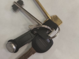 Atslēgu saišķis ar trim atslēgām un melnu elektronisko atslēgu piekariņu. Divas atslēgas ir garas seifa vai slēdzeņu tipa atslēgas – viena zeltītā, otra sudraba krāsā. Trešā ir automašīnas vai cilindriskās slēdzenes atslēga ar melnu plastmasas galviņu. Visi priekšmeti savienoti ar metāla atslēgu riņķi.