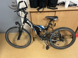 Melns TECHNOBIKE 851 kalnu velosipēds ar zilām detaļām, amortizāciju un ragiem uz stūres, fotografēts no sāna un priekšpuses.