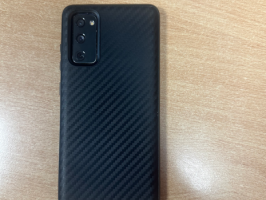 Mobilais telefons "Samsung" ar melnas krāsas vāciņu, uz kura sāniem uzraksts "Rhinoshield”.