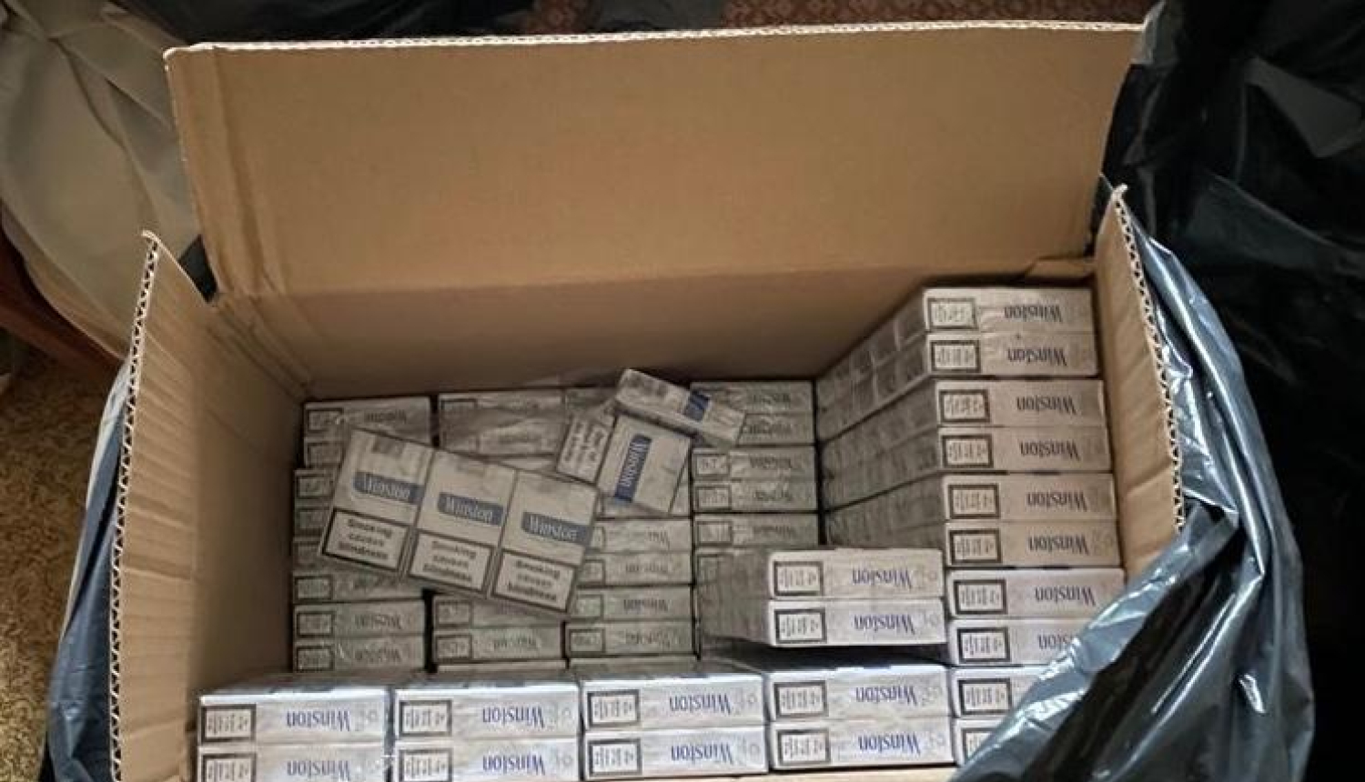 Atvērta kartona kaste, kurā redzami salikti cigarešu "Winston" bloki