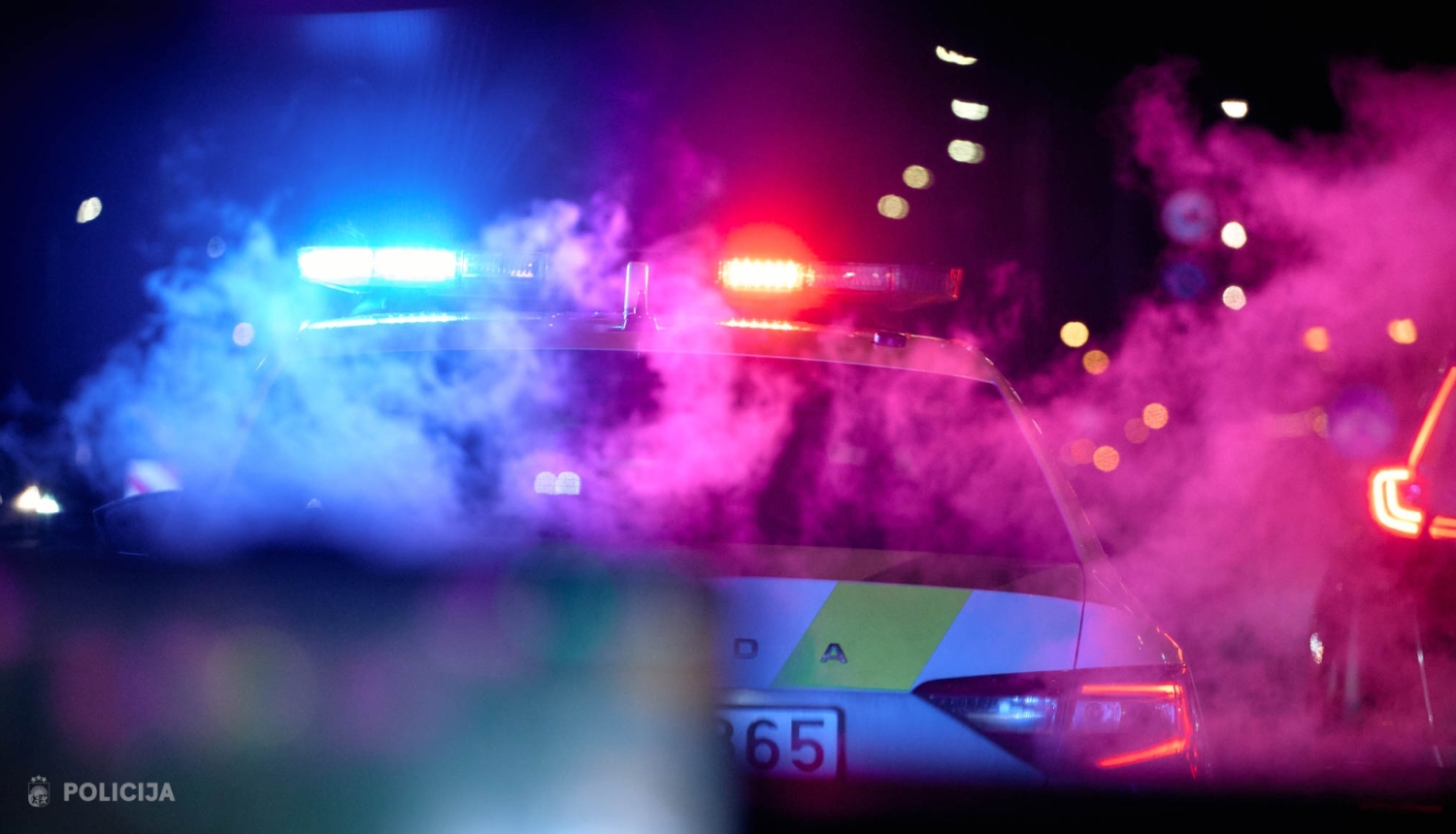 Tumšā diennakts laikā redzama Valsts policijas automašīna ar ieslēgtām zilām un sarkanām bākugunīm. Apkārt auto redzami krāsaini gaismas atspīdumi un dūmi, fonā, izplūdušas pilsētas gaismas