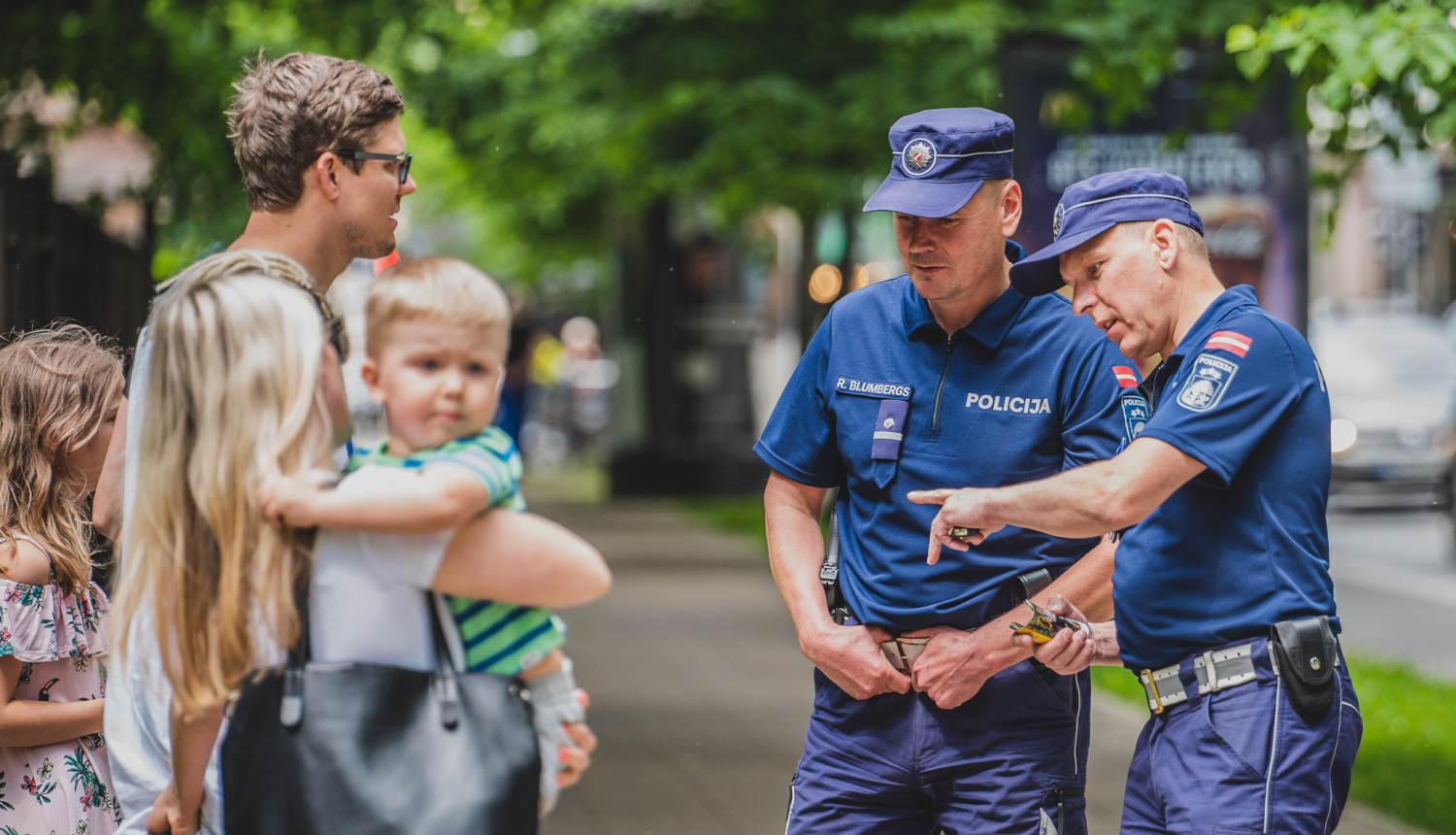 Divi policisti uz ielas komunicē ar pieaugušu vīrieti, sievieti un 2 bērniem