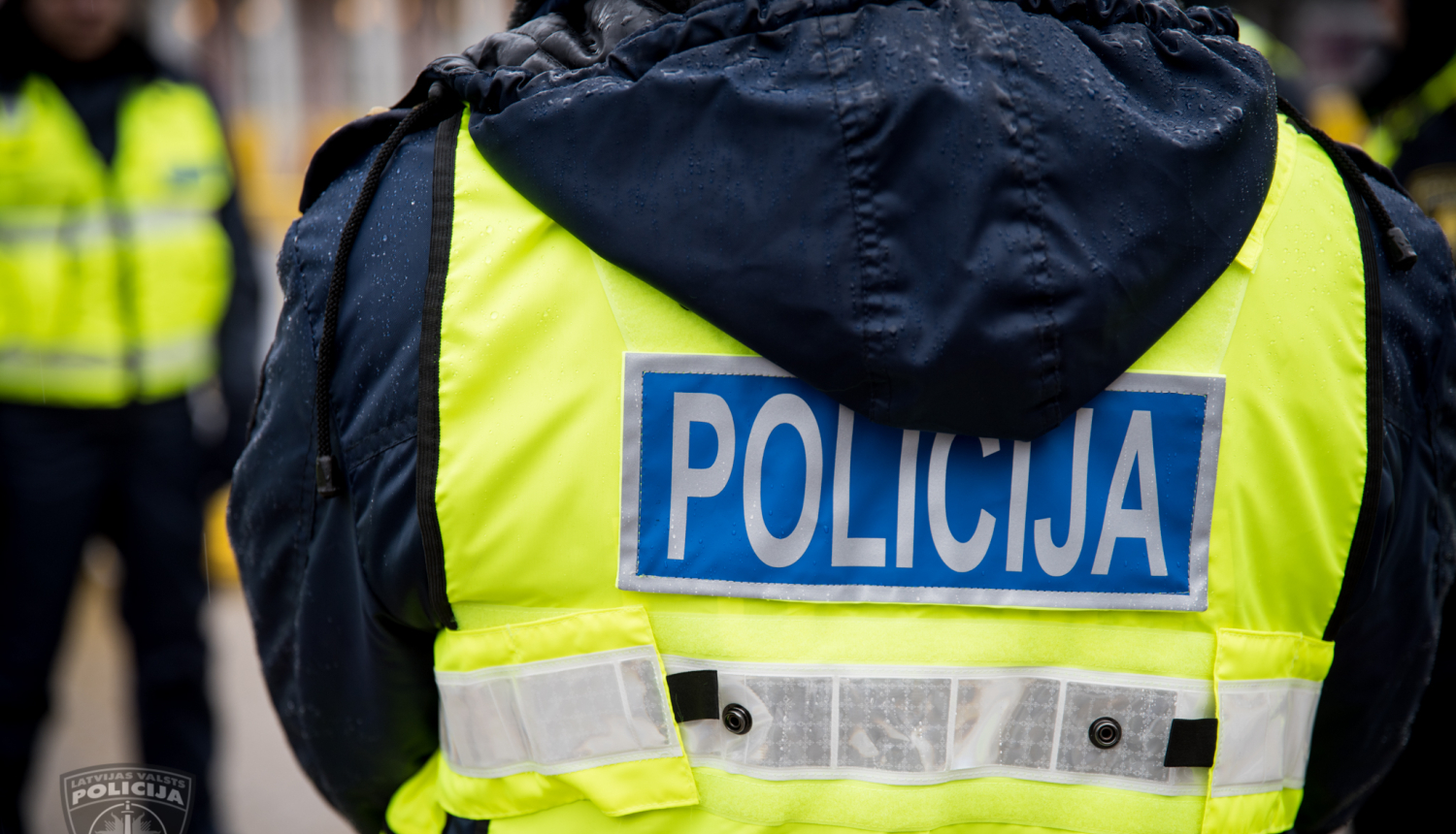 Policists nofotografēts no mugurpuses, fonā redzams stāvam vēl viens policists 