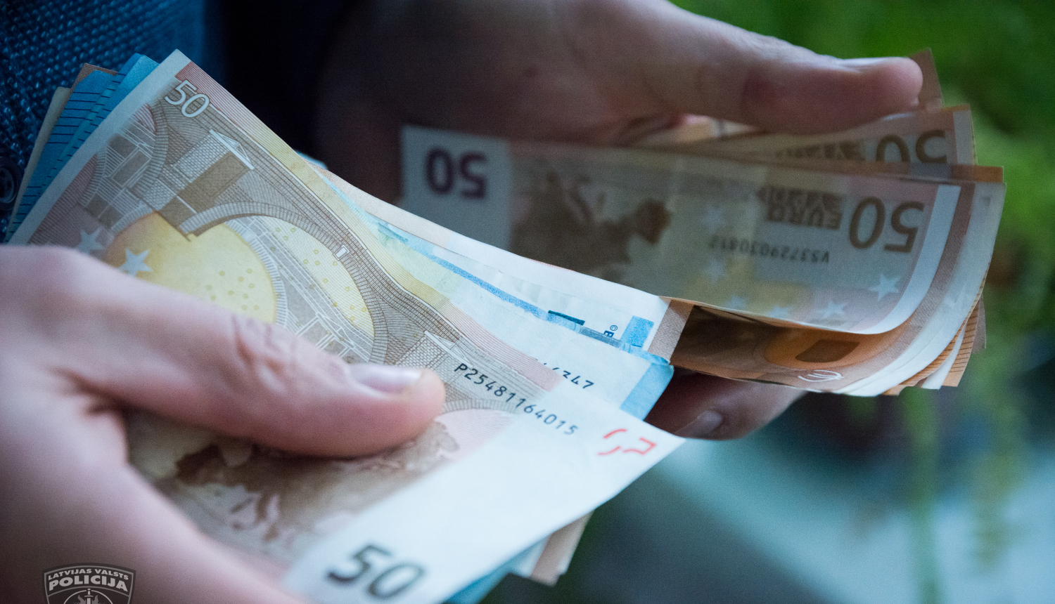 Redzamas 2 cilvēka rokas, kas skaita naudas banknotes. Redzami 50 un 20 eiro nomināli