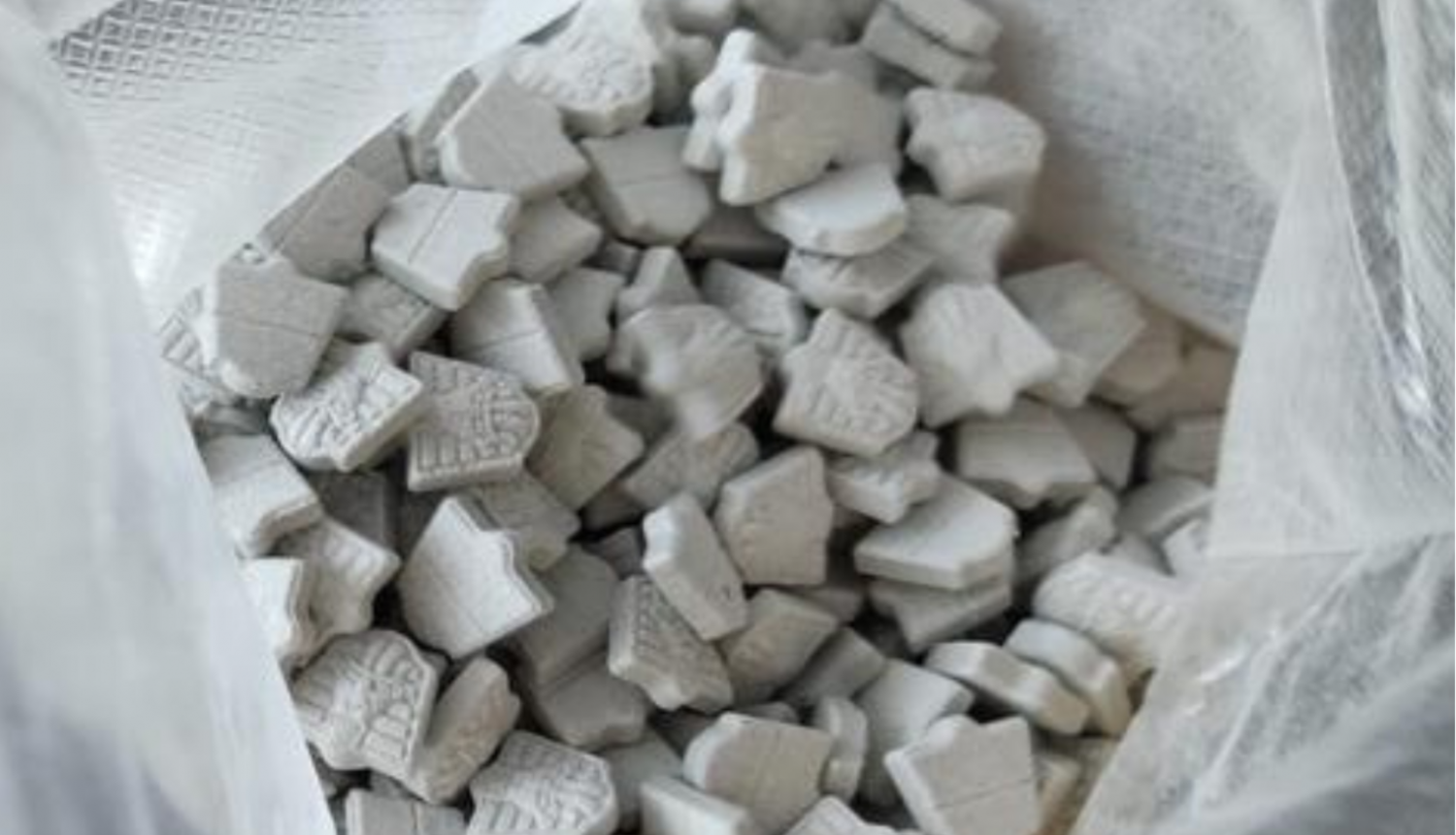 Atvērts polietilēna maiss un tajā redzamas daudz pelēkas MDMA tabletes 