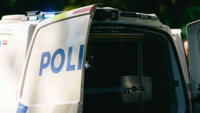 Atvērtas Valsts policijas transportlīdzekļa aizmugurējās durvis ar redzamu uzrakstu “POLICIJA” un ieslēgtām zilajām bākugunīm