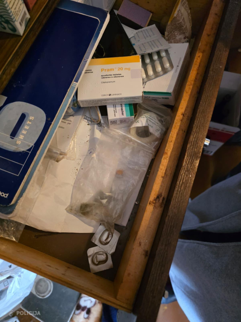 Atvilktnē redzami dažādi medikamentu iepakojumi, tablešu blisteri un plastmasas maisiņš ar augu izcelsmes vielu