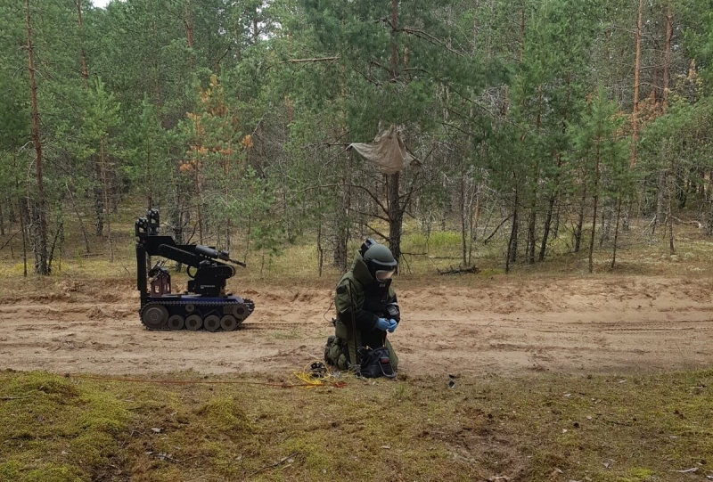 Valsts policijas pretterorisma vienības OMEGA sapieris tērpā. Aizmugurē robots.