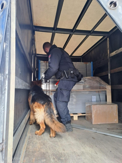 Valsts policijas kinologs kopā ar dienesta suni pārbauda kravas nodalījumu, kurā atrodas iepakotas kastes un paletes