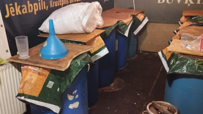 Zilas plastmasas mucas, pārsegtas ar finiera gabaliem, priekšplānā alumīnija kanna, fonā pie sienas operas izrādes "Sikspārnis" platāts un uzņēmuma "Vincents" reklāma  