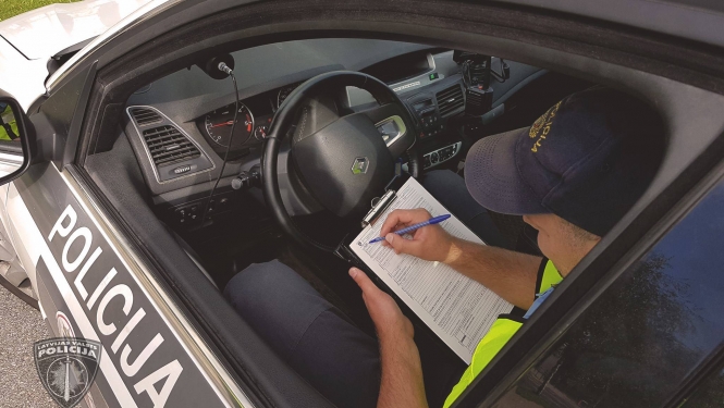 Policijas mašīnā sēž pie stūres policists un aizpilda dokumentus