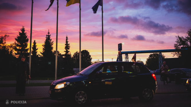 Automašīna, kurai fonā ir saullēkts un karogi