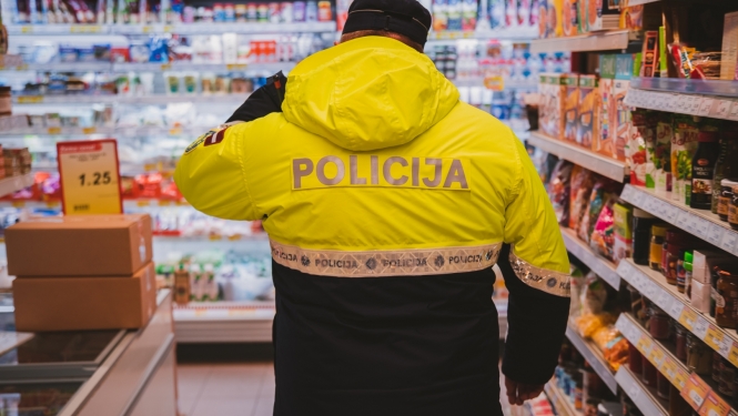 Policists formā no mugurpuses, atrodas veikalā. Vienā malā plaukti, priekšā fonā redzama piena produktu nodaļa