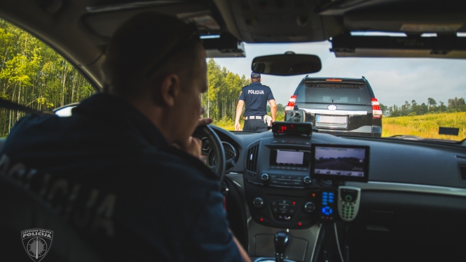 Skats policijas mašīnas iekšpusē, pie stūres sēž policists dienesta apģērbā