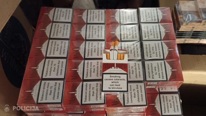 liels daudzums cigarešu paciņu, kas sakrautas kastē vairākās rindās, virspusē novietotas arī dažas atsevišķas cigaretes