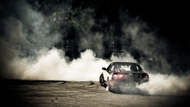 Mašīna, kas "drifto", fonā redzami dūmi