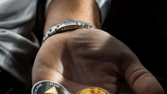 Vīrieša rokas plaukstā trīs kriptovalūtas monētas