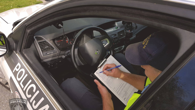 Policijas mašīnā sēž pie stūres policists un aizpilda dokumentus