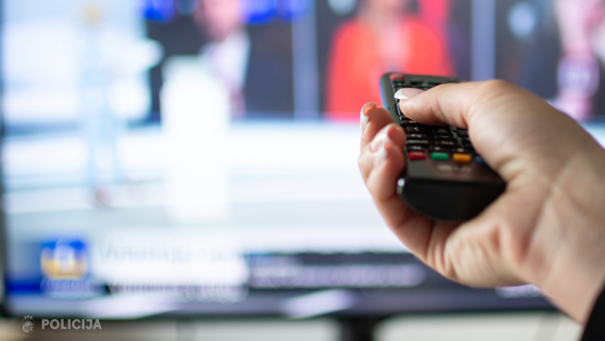 cilvēks tur rokās pulti pret televizoru