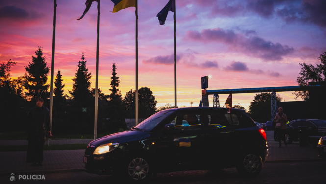 Automašīna, kurai fonā ir saullēkts un karogi