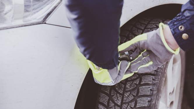 Redzamas rokas, kuras arvauto riepu protektoru dziļuma mērītāju mēra gaišas krāsas auto riepu protektoru dziļumu 