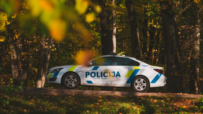 Policijas automašīna stāv uz ceļa, visapkārt koki, krāsainās rudens lapās