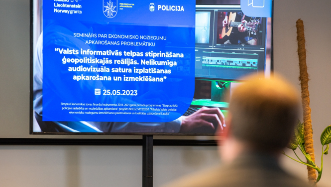 Cilvēks pavērsis muguru pret kameru, skatās uz ekrāna kurā redzama prezentācija