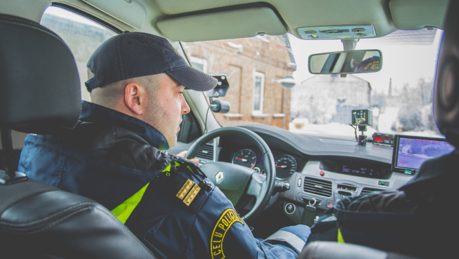 Ceļu policijas darbinieks automašīnā pie stūres, fotografēts no aizmugurējās sēdvietas