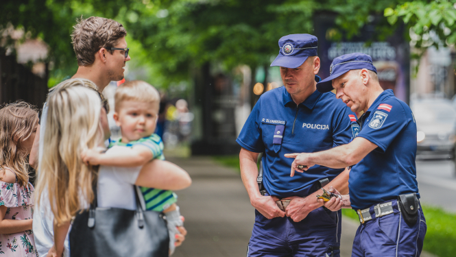 Divi policisti uz ielas komunicē ar pieaugušu vīrieti, sievieti un 2 bērniem