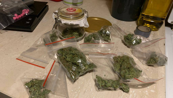 Uz galda caurspīdīgi plastikāta maisiņi ar marihuānu un uz svariem maisiņš ar rozā tabletēm