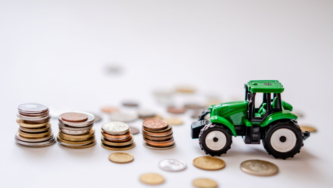 Zaļš rotaļu traktors, kuram priekšā četras monētu kaudzītes un atsevišķas monētas izbārstītas pa gaišu galda virsmu