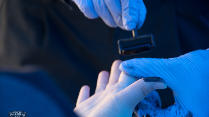 Eksperta rokas zilos gumijas cimdos un kādas personas roka, no kuras tiek noņemti pirkstu nospiedumi