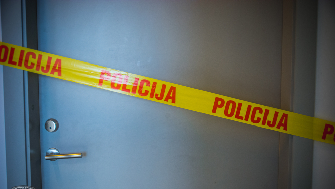 Pelēkas durvis, kurām priekšā novilkta dzeltena lenta, uz kuras ar sarkaniem burtiem uzrakstīts "Policija"