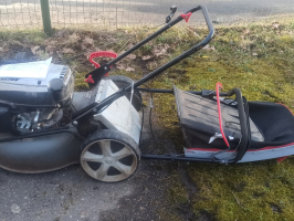 zāles pļāvējs ar savācējrozu novietots uz zāles seguma