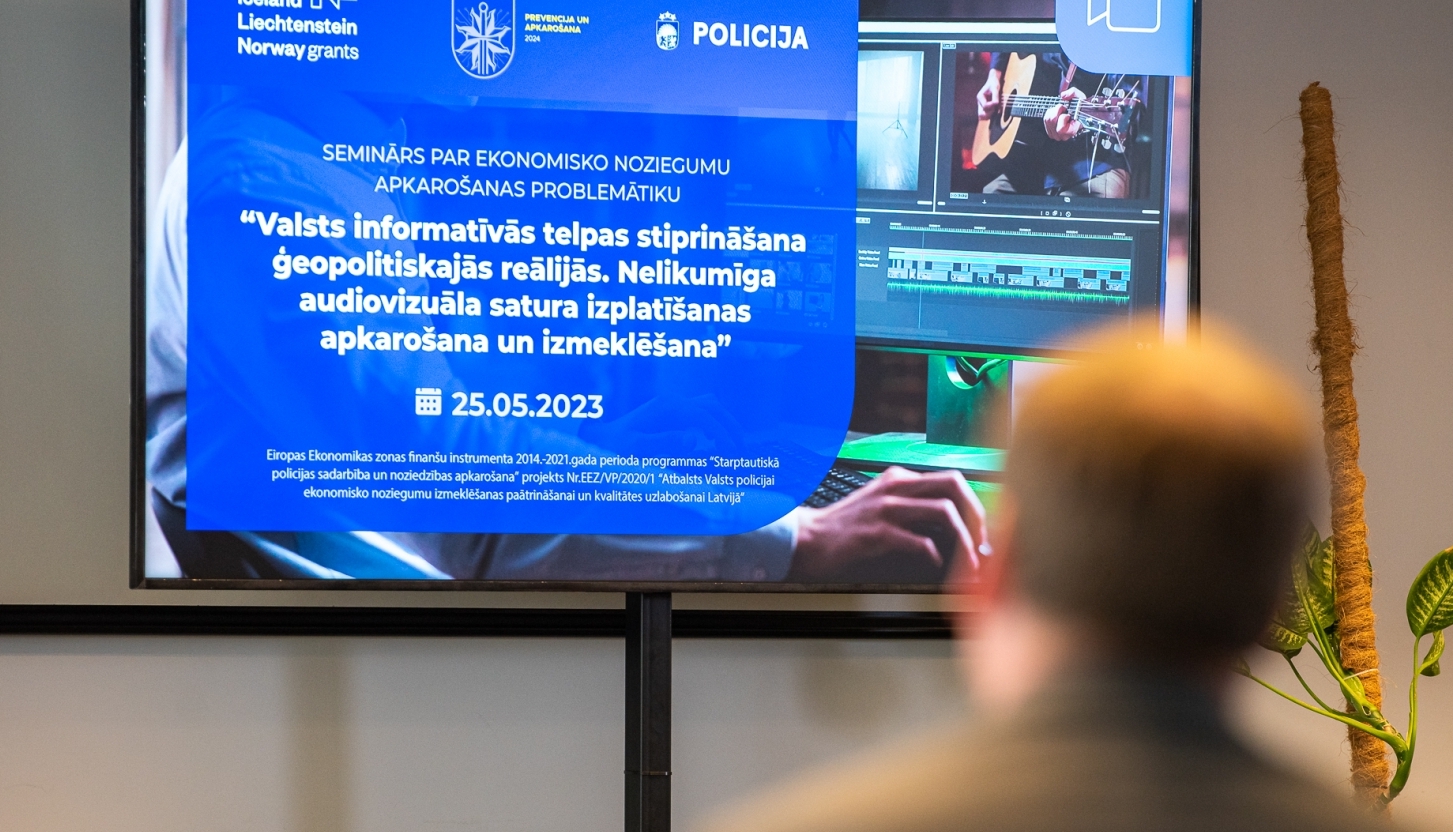 Cilvēks pavērsis muguru pret kameru, skatās uz ekrāna kurā redzama prezentācija