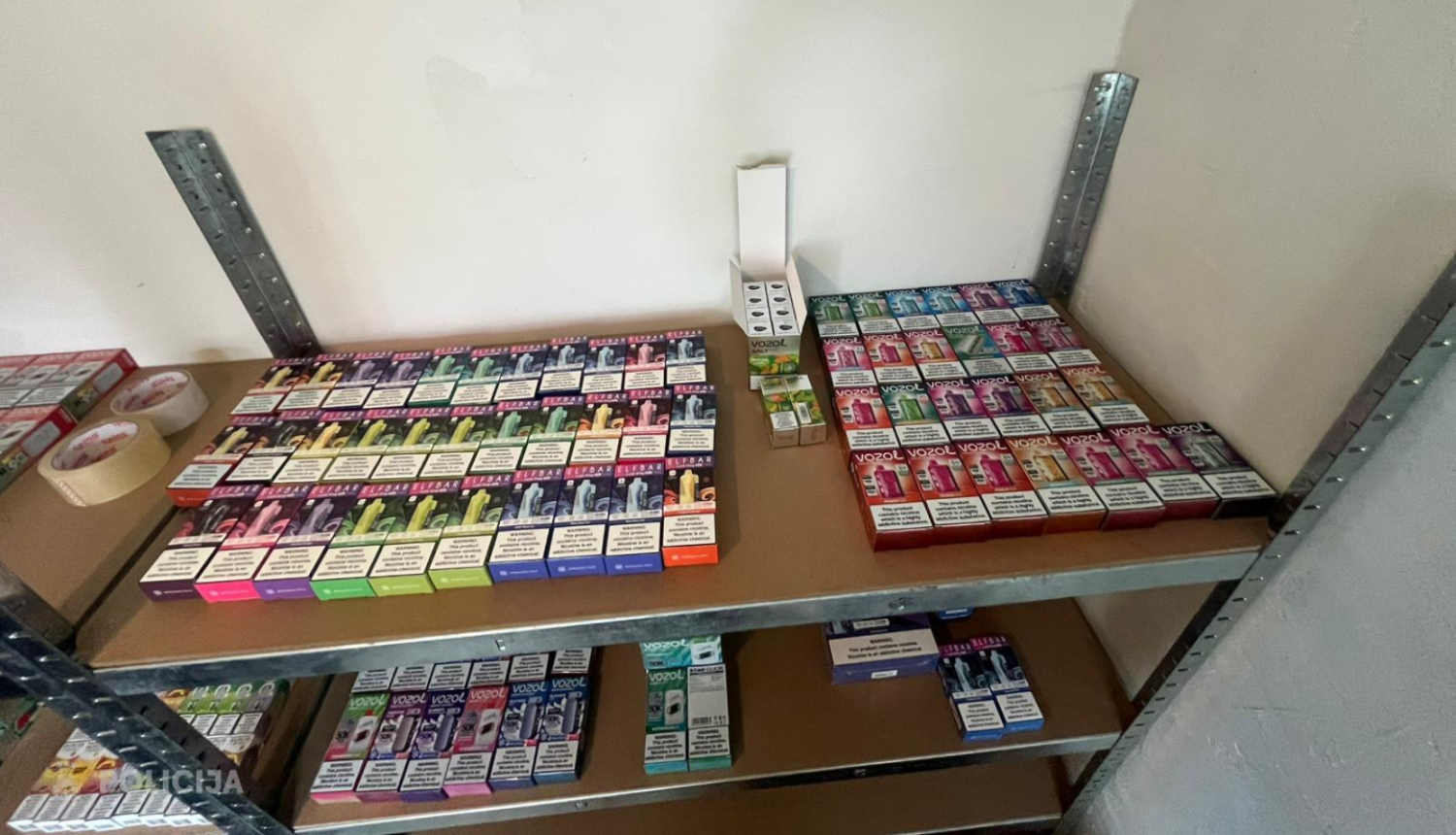 Metāla plauktā novietotas daudzas elektronisko cigarešu un veipu iepakojumu kastes dažādās krāsās, sakārtotas vairākās rindās uz diviem plauktiem