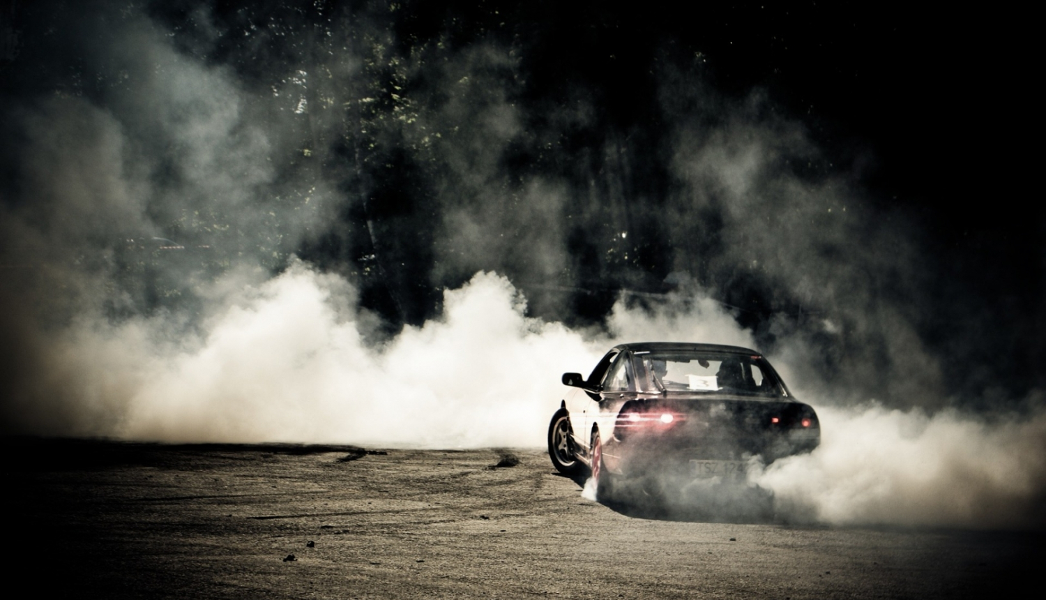 Mašīna, kas "drifto", fonā redzami dūmi