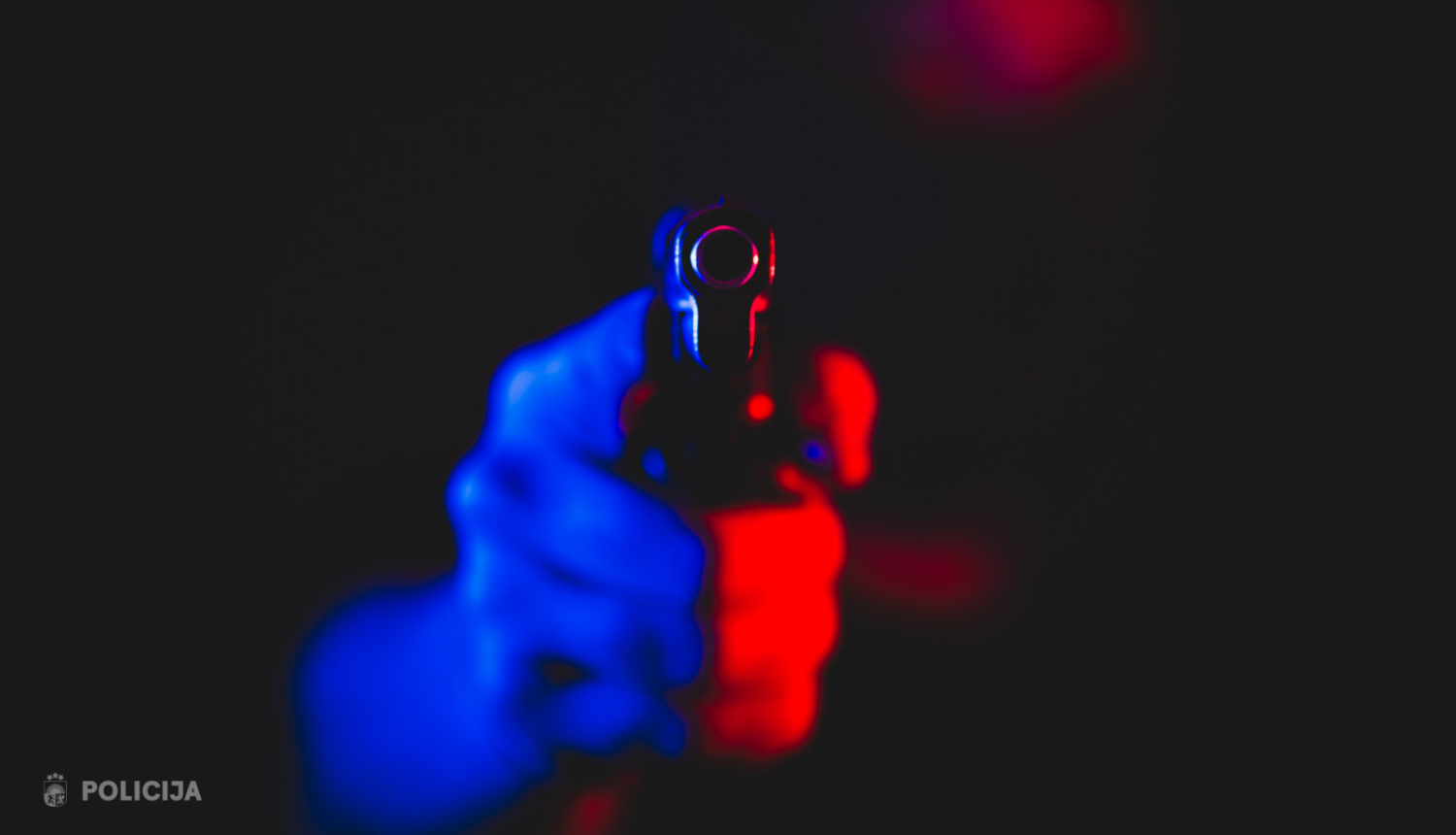 Vīrietis tur rokās ieroci, tas ir izgaismots ar zilu un sarkanu gaismu