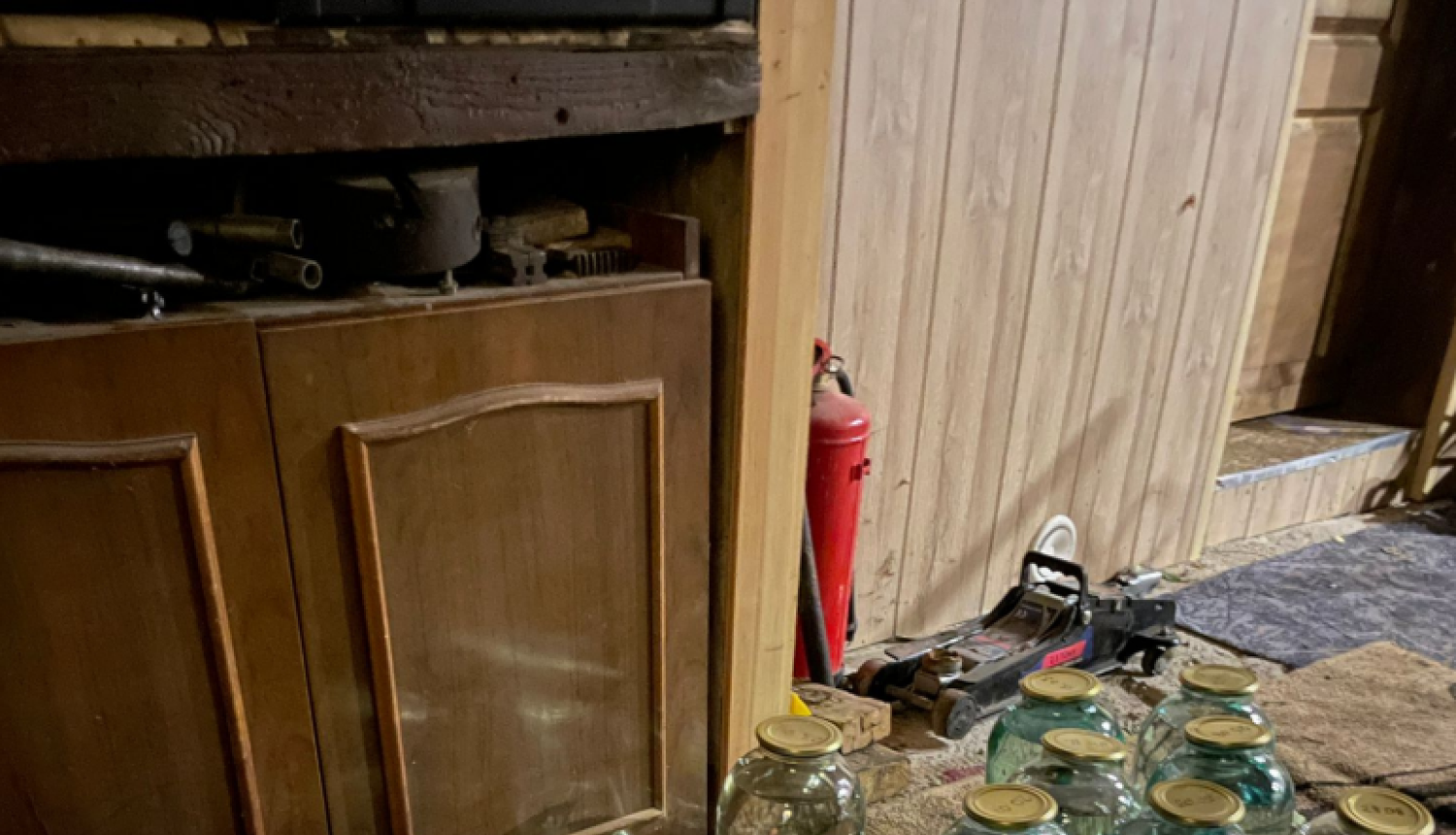 Uz grīdas vairākas trīslitru burkas ar caurspīdīgu šķidrumu un zilā kastē pudeles ar tumšu šķidrumu