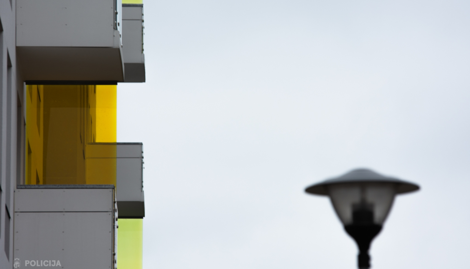 Daudzdzīvokļu mājas balkoni attēla kreisajā pusē un labajā pusē laterna 