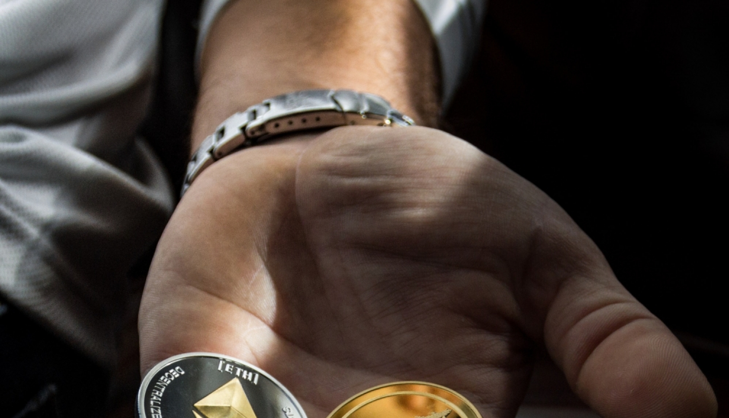 Vīrieša rokas plaukstā trīs kriptovalūtas monētas