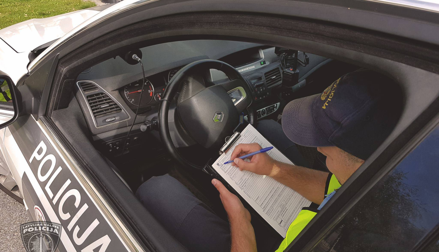 Policijas mašīnā sēž pie stūres policists un aizpilda dokumentus