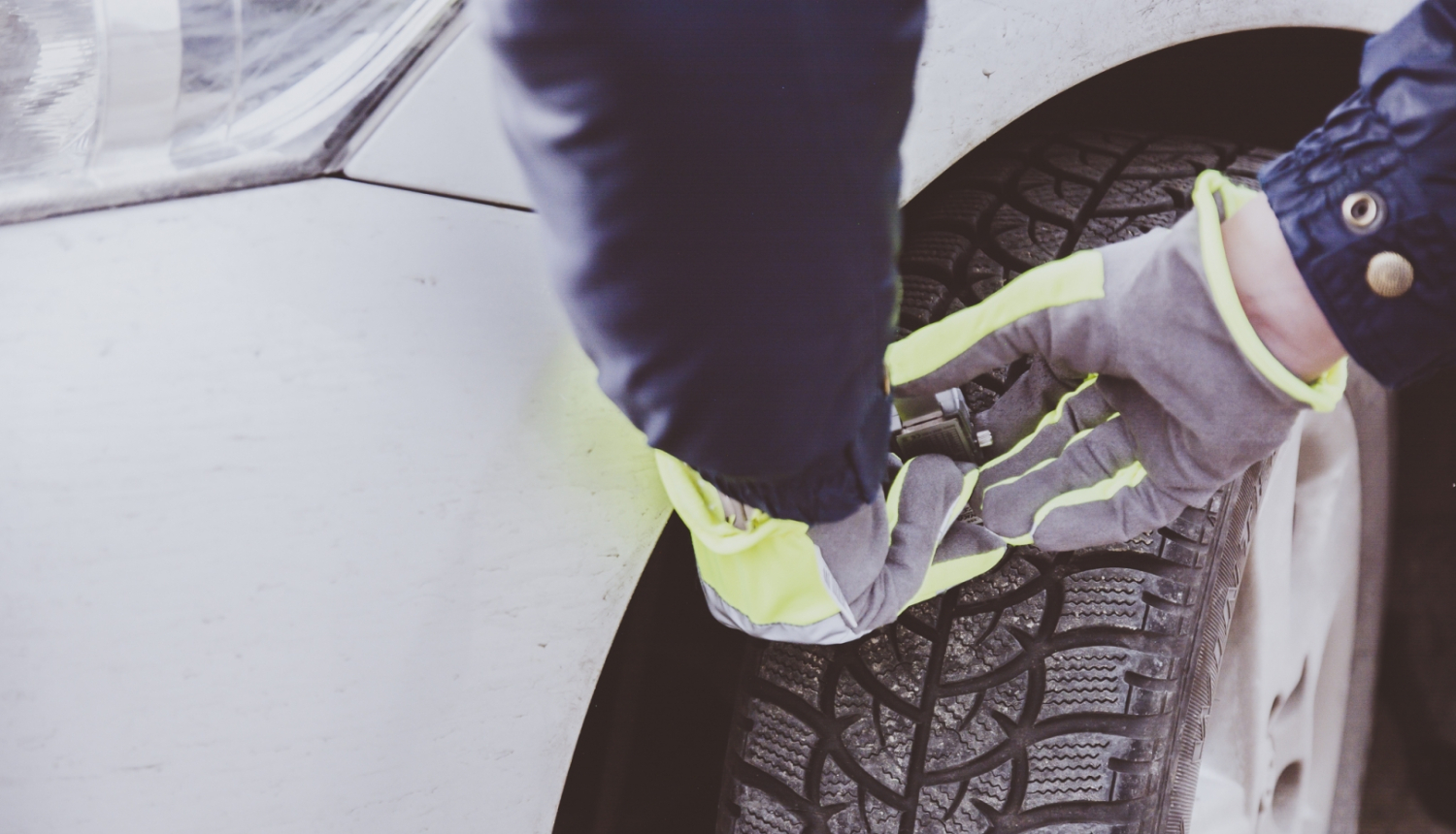 Redzamas rokas, kuras arvauto riepu protektoru dziļuma mērītāju mēra gaišas krāsas auto riepu protektoru dziļumu 